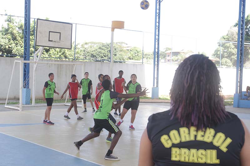 adolescente jogando bola em uma quadra e uma mulher em pé olhando