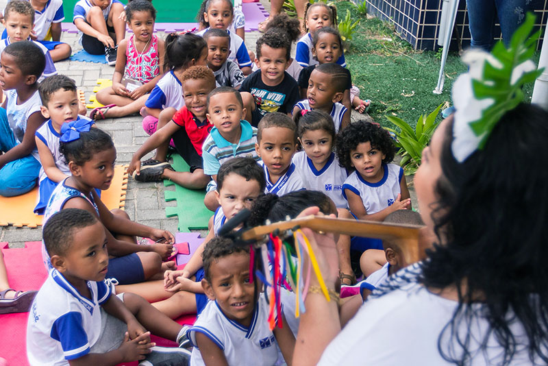 Foto de professora tocando violão para crianças da rede municipal.